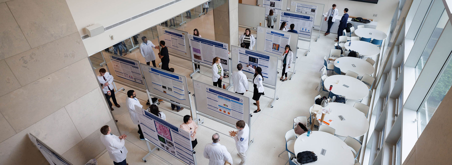 Wide view of medical poster session with participants presenting and discussing research. Wide view of medical poster session with participants presenting and discussing research.